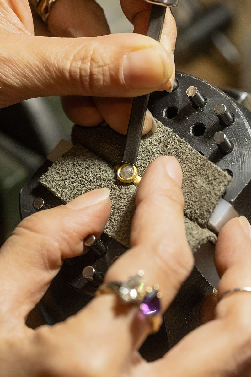 Macro shot of a ring in progress on the bench: prongs, loupe, and hand tools visible